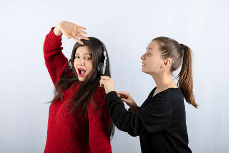 Young girl calling brunette woman in headphones on white background