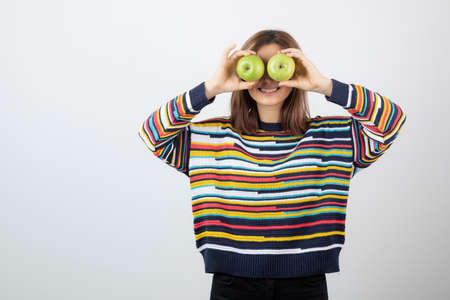 Young woman in casual outfit holding green apples in front of eyesの写真素材