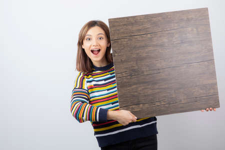 Image of a young woman model standing and holding wooden backgroundの写真素材