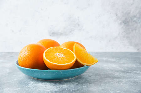 A plate full of sliced and whole juicy orange fruits on stone background