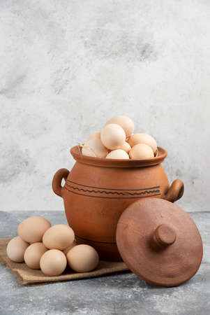 Clay pot full of raw chicken eggs on marble backgroundの写真素材