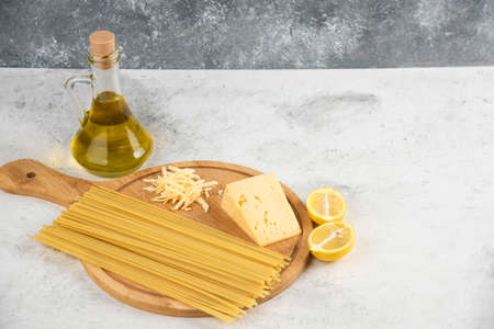 Raw spaghetti, oil, lemon and cheese on white table