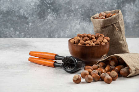 Bowl of organic hazelnut kernels and shelled hazelnuts on marble background