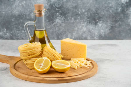 Spaghetti nests, oil, lemon and cheese on wooden board