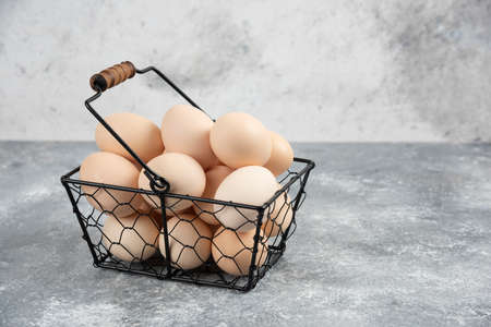 Metal basket of fresh organic raw eggs on marble surfaceの写真素材