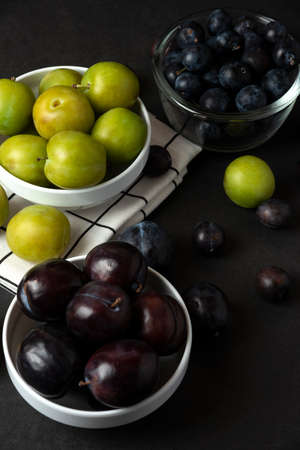 Black and green plums in white ceramic saucer in the kitchenの写真素材