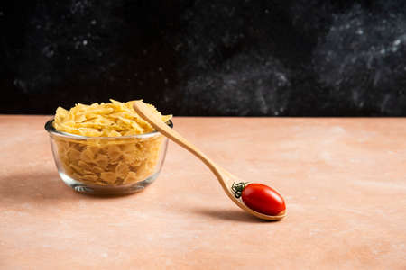 Bowl of raw pasta and tomato on orange tableの写真素材