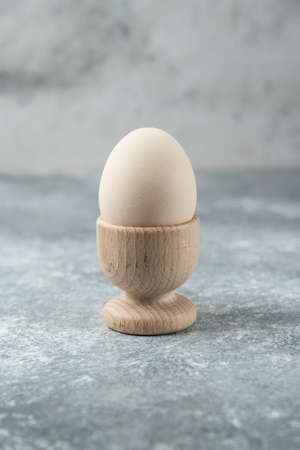Raw egg in wooden bowl on marble table