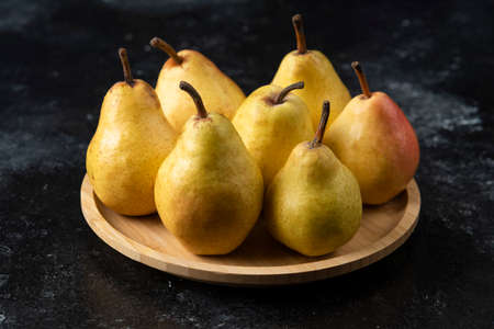 Wooden plate of tasty yellow pears on black surfaceの写真素材