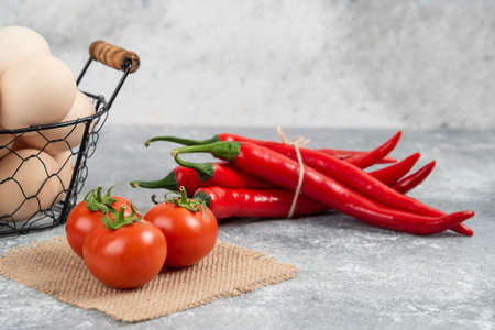 Basket of fresh uncooked eggs, chili peppers and tomatoes on marble backgroundの写真素材