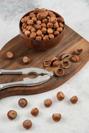 Wooden bowl of unpeeled organic hazelnut kernels on cutting board