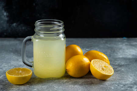 A glass jar of tasty lemon juice and slices on a marble background