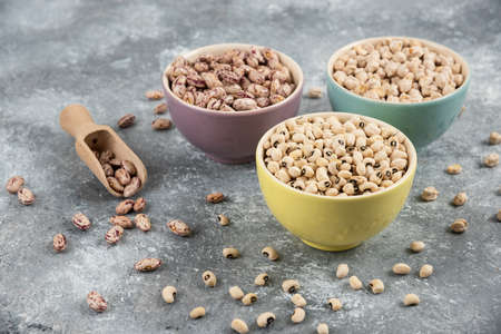 Bowls of various uncooked beans on marble surface