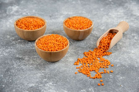 Wooden bowls of red raw lentils on marble background