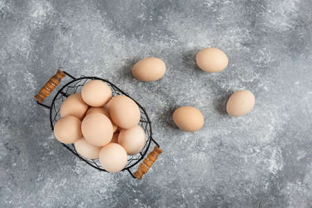 Wicker basket of raw organic eggs on marble background
