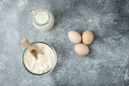 Flour, raw eggs and milk on marble background
