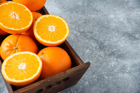 A wooden old box full of sliced and whole juicy orange fruits