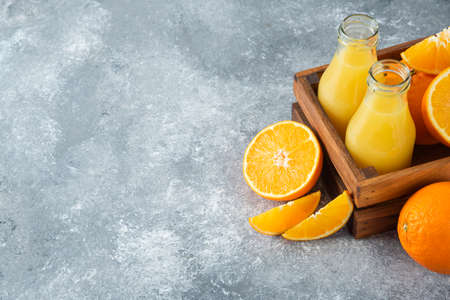 A wooden old box full of orange fruits and glass pitchers of juiceの写真素材