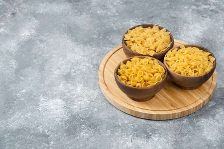 Wooden bowls of raw dry pasta on marble surface