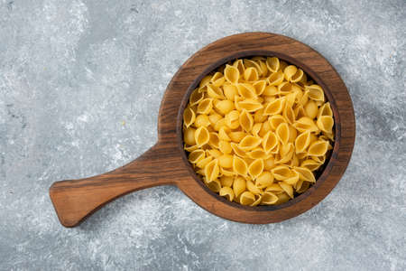 Wooden bowl of raw seashell pasta on cutting boardの写真素材
