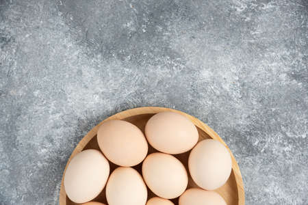 Wooden plate of fresh organic raw eggs on marble surface