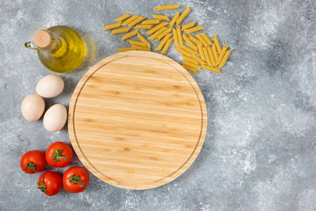 Wooden board of raw dry spaghetti, eggs and tomatoes on marble surfaceの写真素材