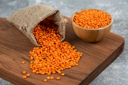 Bowl and sackcloth of red raw lentils on wooden board