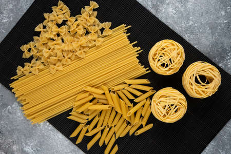 Various uncooked pasta on black bamboo sheetの写真素材