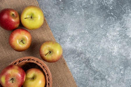 Wicker basket of ripe shiny apples on marble surfaceの写真素材