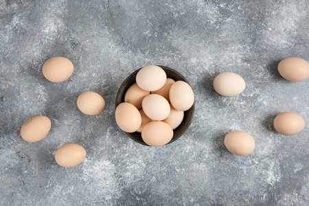 Wooden bowl of organic raw eggs placed on marble surface