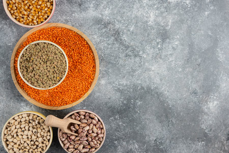 Bowls of various uncooked beans, lentils and corns on marble surface