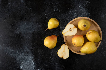 Wooden plate of delicious yellow pears on black surfaceの写真素材