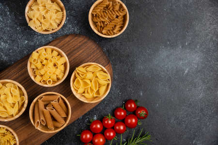 Pasta varieties in wooden cups served with cherry tomatoes and rosemary leavesの写真素材