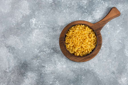 Wooden bowl of raw seashell pasta on cutting board