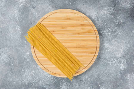 Wooden board of raw dry spaghetti placed on marble surfaceの写真素材