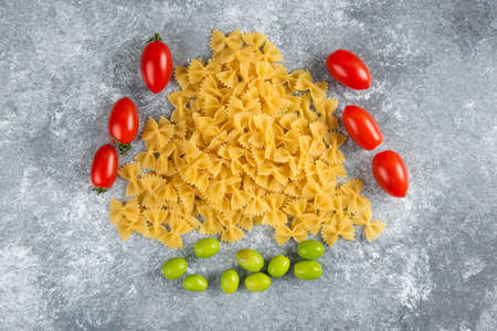 Uncooked farfalle and tomatoes on marble backgroundの写真素材