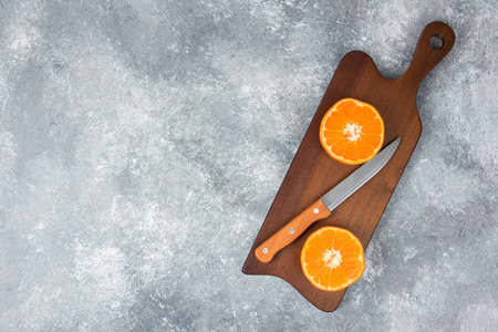A wooden board of juicy slices of orange fruit with a knife on stone backgroundの写真素材