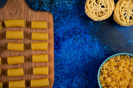 Pasta varieties on a wooden board and in blue cupsの写真素材