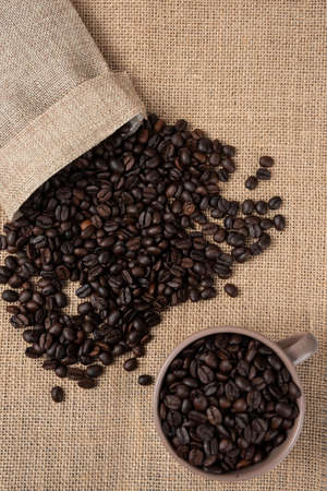 Bunch of medium roasted coffee beans out of sackcloth on marble surface