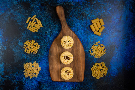Noodle rolls and pasta varieties on a wooden board on blue backgroundの写真素材