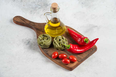 Green tagliatelle, vegetables and olive oil on wooden boardの写真素材