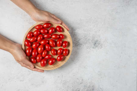 Female hands holding plate of cherry tomatoesの写真素材