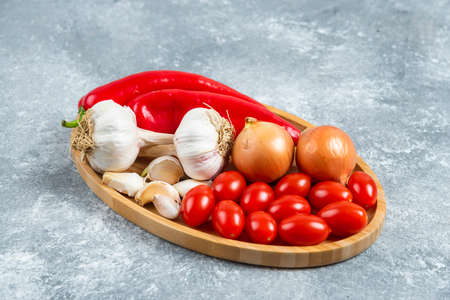 Tomatoes, garlic and peppers on wooden plateの写真素材