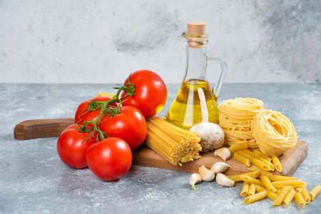 Assortment of raw pasta, olive oil and tomatoes on wooden boardの写真素材