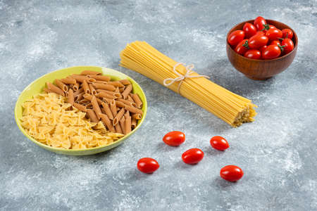 Two kinds of raw pasta on plate with tomatoes and spaghettiの写真素材