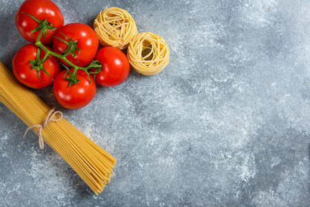 Uncooked spaghetti with fresh red tomatoes on a marble backgroundの写真素材