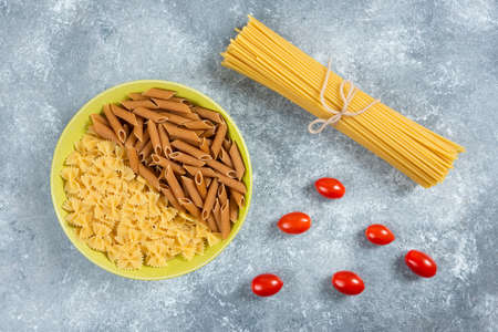 Two types of raw pasta on plate with tomatoes and spaghettiの写真素材