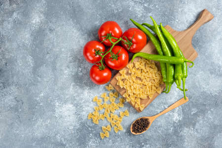 Raw farfalle, tomatoes and chili peppers on wooden boardの写真素材
