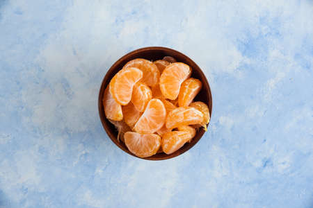 Top view of Mandarin slices in wooden bowl on blue backgroundの写真素材