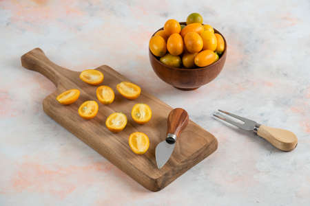Whole kumquats in bowl and half cut kumquats on wooden cutting boardの写真素材